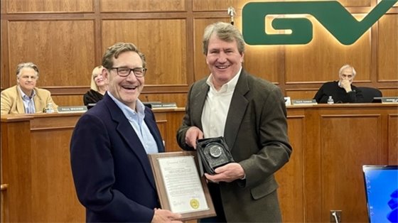 Brian Strandes and Mayor George Lantz hold a plaque in Council Chambers.