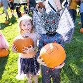 Two kids in costumes holding pumpkins.