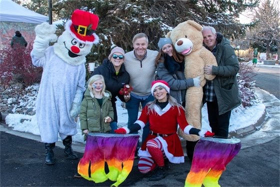 Snowman character and flag dancer poses with family holding large stuffed bear at Mayor's Holiday Lighting