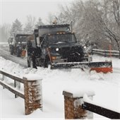 Two snow plows drive down a street during a winter storm.