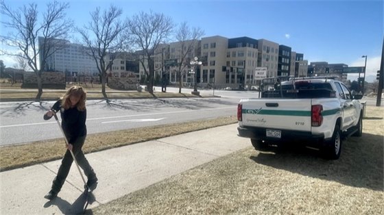 A code enforcement officer sweeps debris from a sidewalk next to a City vehicle.