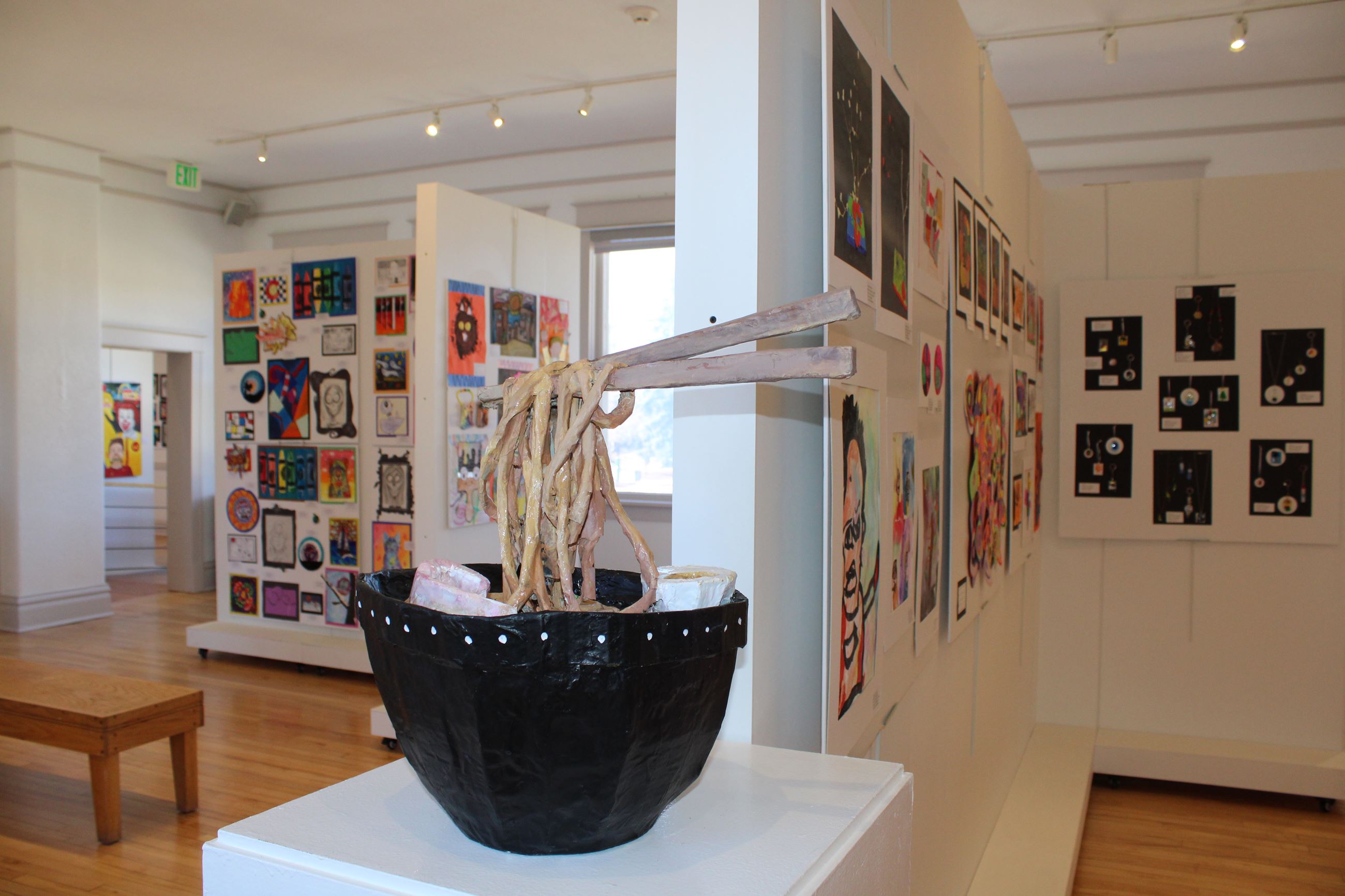 Image of a kid's sculpture and children's art hung in a gallery. 